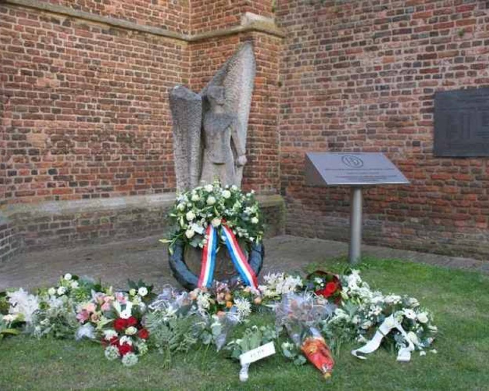 Herdenkingsmonument met krans en bloemen voor een kerkmuur