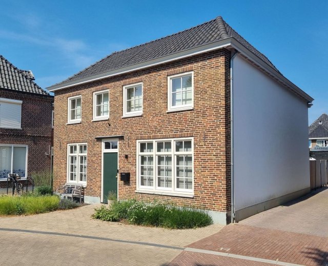 Karakteristieke woning met witte zijgevel, groene deur en veel ramen