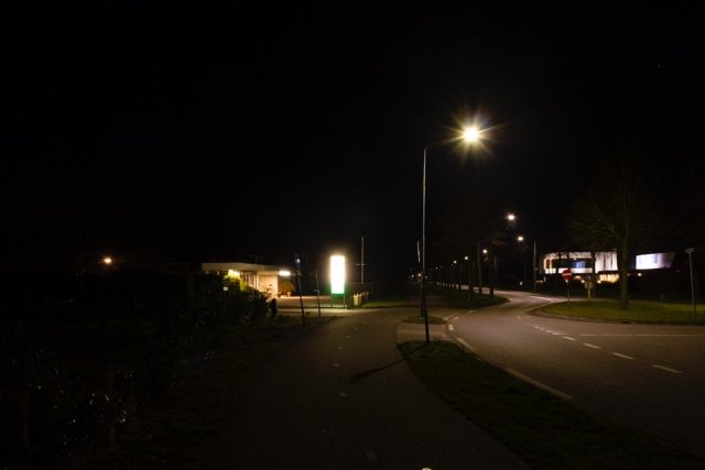 Spinnerij in Aalten. Rechts een verlicht pand dat van verre zichtbaar is en waardoor het op de weg donker lijkt. Links een reclamebord dat niet meer te lezen is.