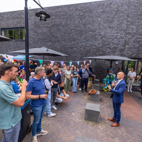 Het met vlaggetjes versierde plein voor het gemeentehuis staat vol met tientallen mensen, ze worden toegesproken door burgemeester Jouke Douwe de Vries.