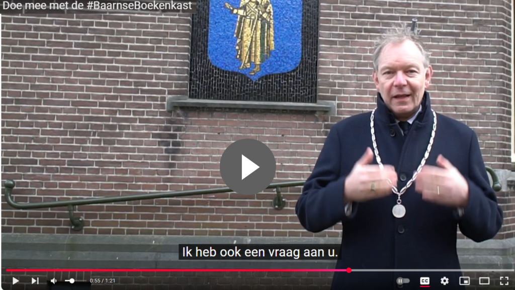 Burgemeester Mark Röell van Baarn staat voor een camera en roept op tot het delen van verhalen voor de Baarnse Boekenkast. Klik op de foto om de video af te laten spelen