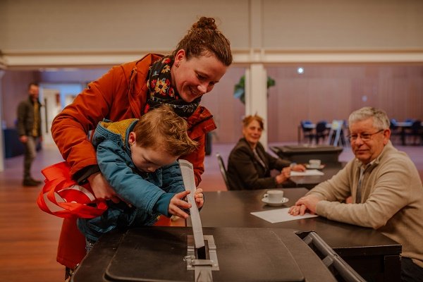 Foto van moeder en kind met stembiljet in 't Hof van Sjapubik