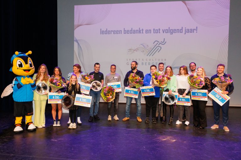 Winnaars van de sport-cultuurprijs staan met hun cheque en bos bloemen op het podium