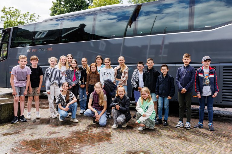 Jeugdgemeenteraadsleden zitten gehurkt en staan voor een bus