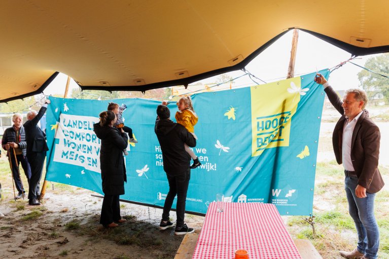 Wethouder Mathijs Kuijken staat met de mensen op de bouw de vlag vast te houden om de opening te vieren