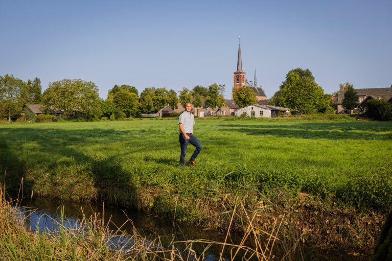 Collega Jos van Mierlo in een weiland met op de achtergrond kern 't Loo