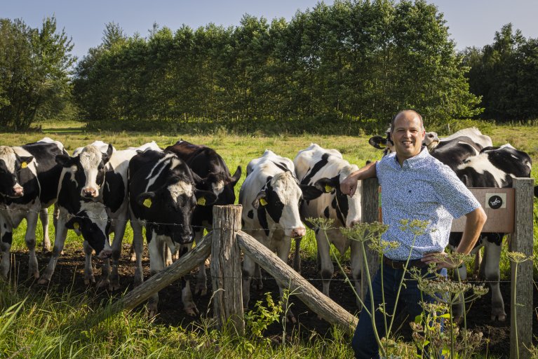 Jos van Mierlo staat tegen een hek geleund bij een wei met koeien