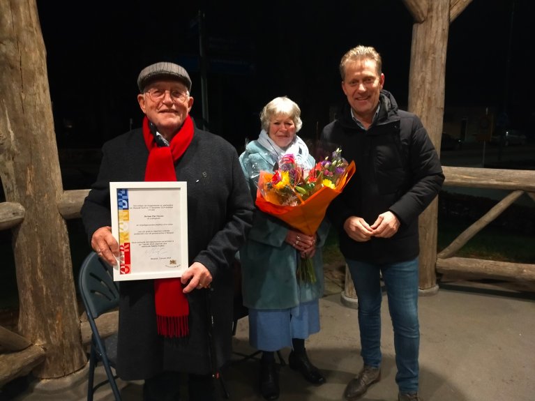 Piet Theuws, zijn vrouw en wethouder Mathijs Kuijken staan bij elkaar met de vrijwilligersonderscheiding in de handen van Piet.