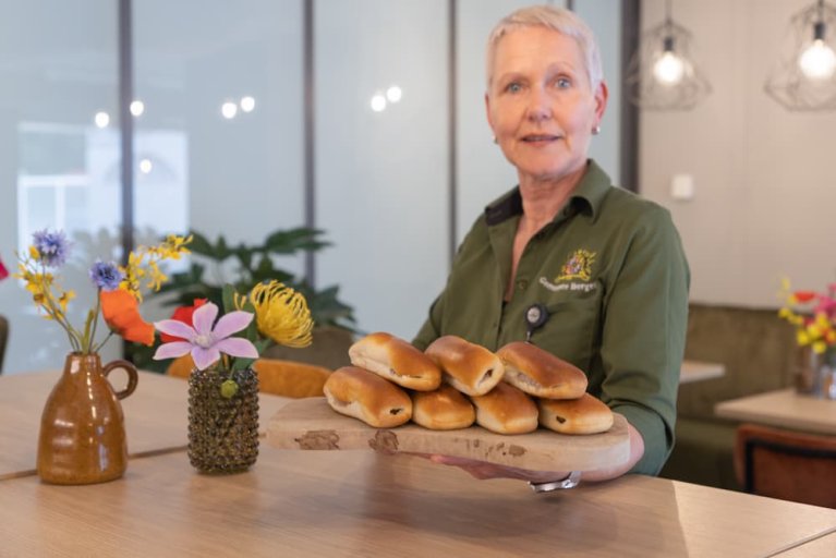 Een collega van het bedrijfsrestaurant presenteert worstenbroodjes op een serveerplank