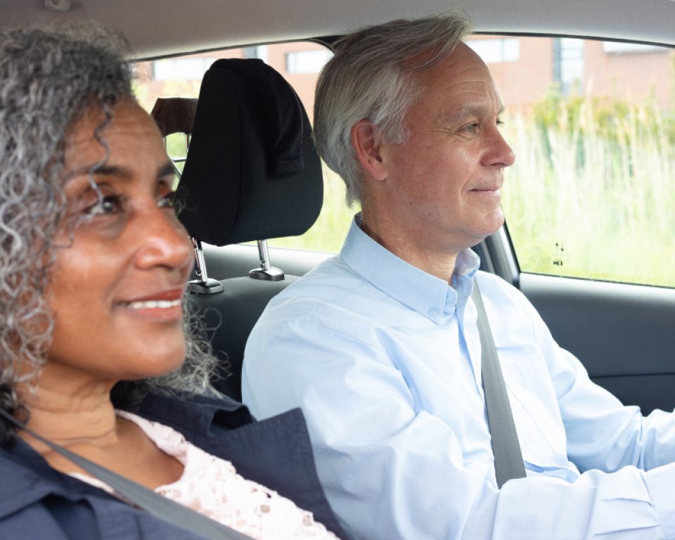 Oudere man zit aan het stuur, vrouw zit ernaast in de auto