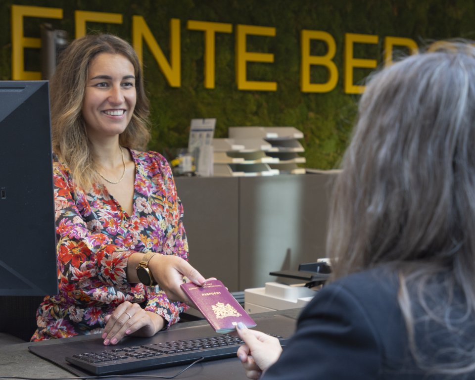 Medewerker aan de balie overhandigt paspoort aan bewoner