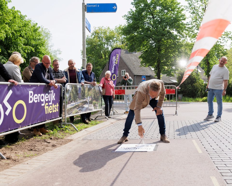 Wethouder Mathijs Kuijken schildert logo Bergeijk Fietst op het fietspad