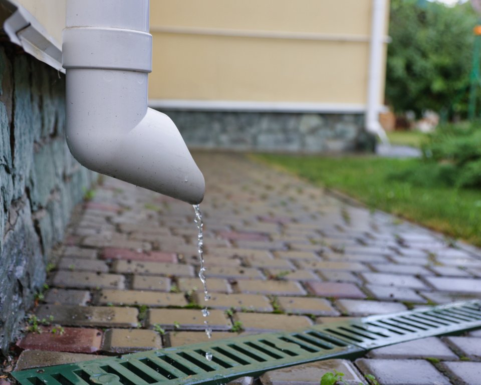 Regenpijp waar water uit loopt en in een rooster in de grond terecht komt