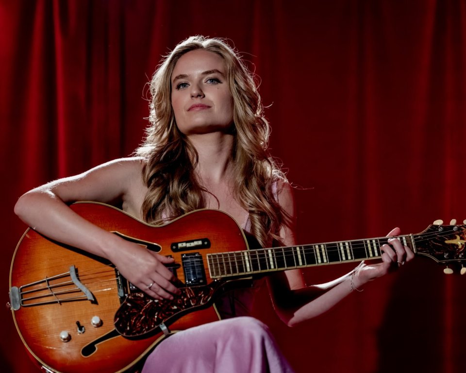 Rosa Spruit zit met een gitaar op een stoel