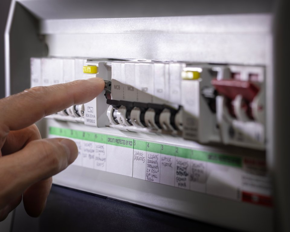 Iemand wijst een schakelaar in de meterkast aan