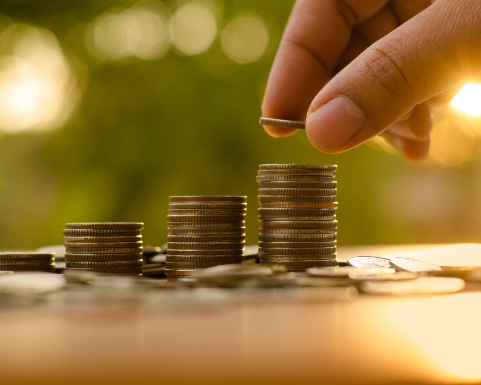 Een hand legt een muntje bovenop een stapel muntjes