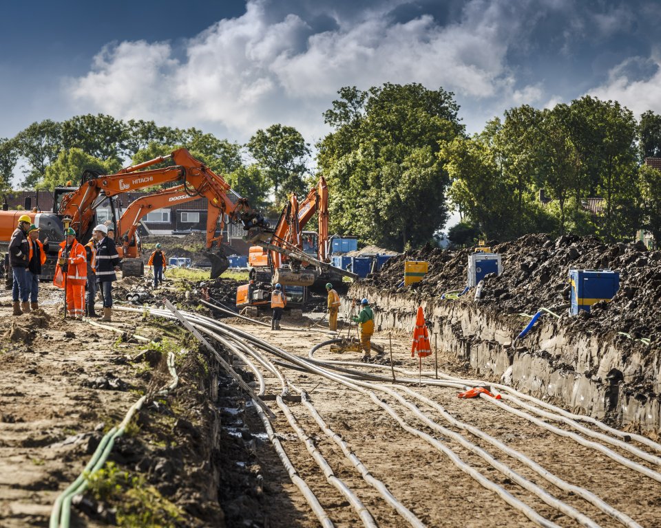 Kabels in de grond met graafmachine en werklui erbij