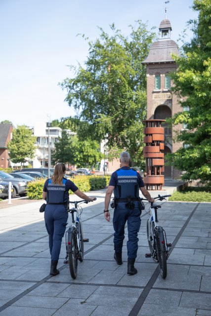 Twee boa's lopen met de fiets aan de hand voor het gemeentehuis