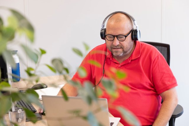 Mannelijke collega aan zijn bureau achter een laptop met een koptelefoon op