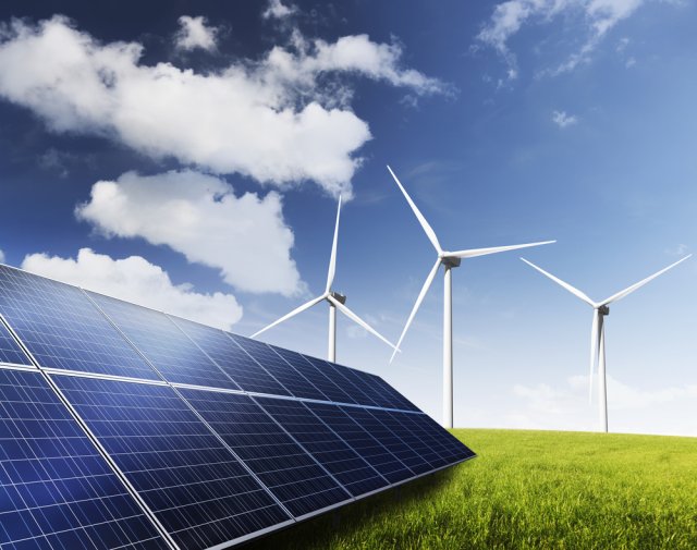 Drie windmolens staan in het gras naast zonnepanelen 