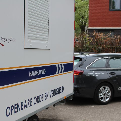 De kar van team Handhaving, met de tekst 'openbare orde en veiligheid' duidelijk in beeld, achter een auto met het gemeentelogo en dezelfde tekst.