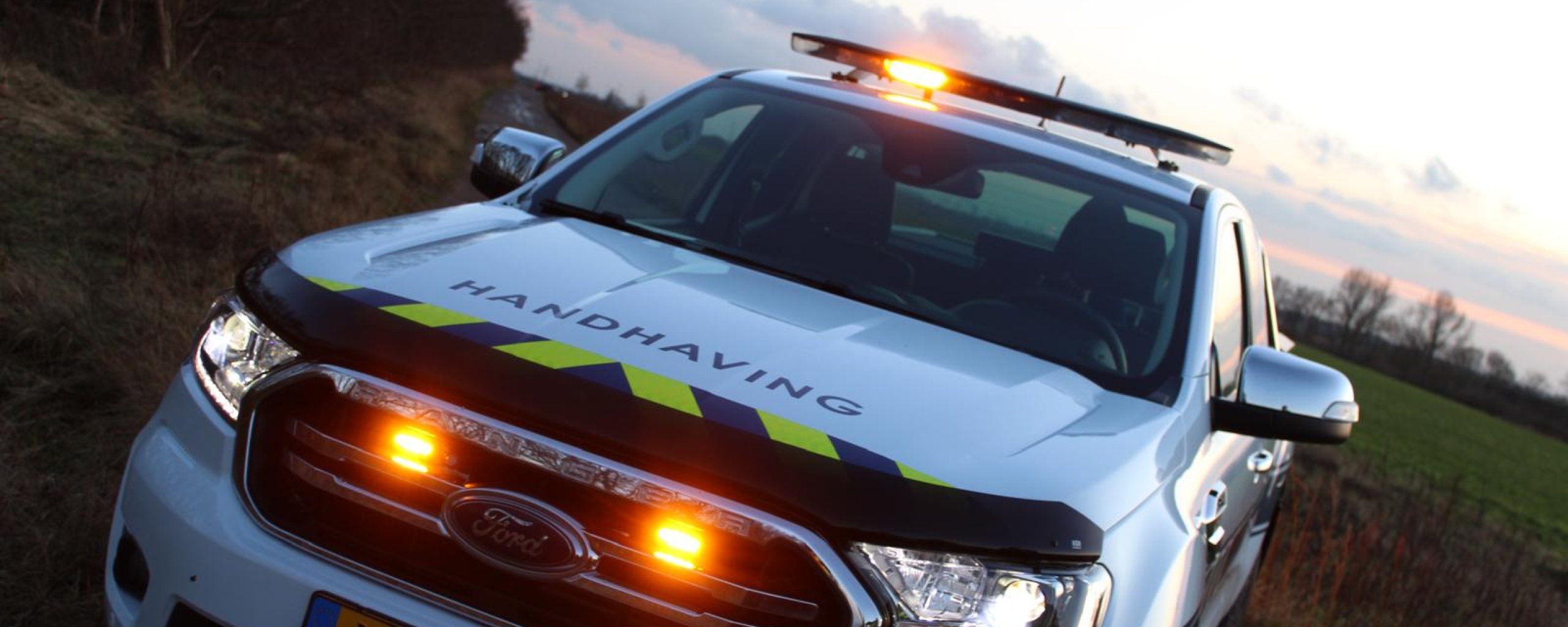 Auto van team Handhaving in het schemerdonker in de natuur geparkeerd, met alarmlichten aan de bovenkant en voorzijde van de auto.