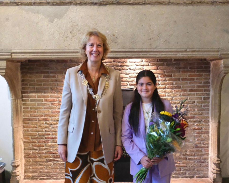 Burgemeester met naast haar de nieuwe kinderburgemeester, zij houdt een bos bloemen vast.