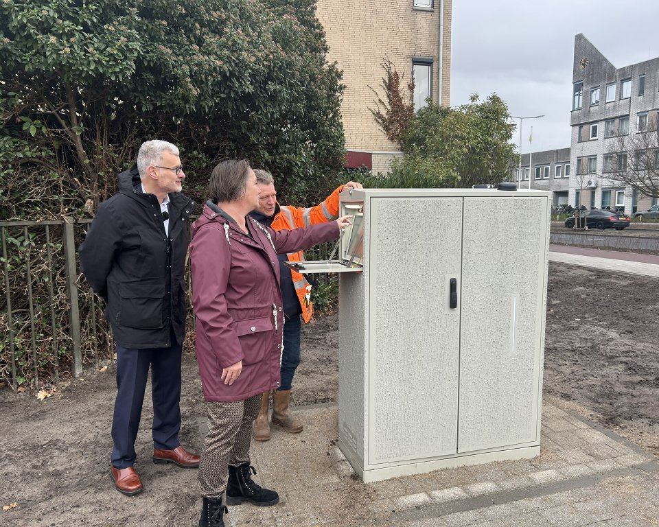 Drie mensen naast een elektriciteitskast, de middelste drukt op de knop om het kruispunt officieel te heropenen. 
