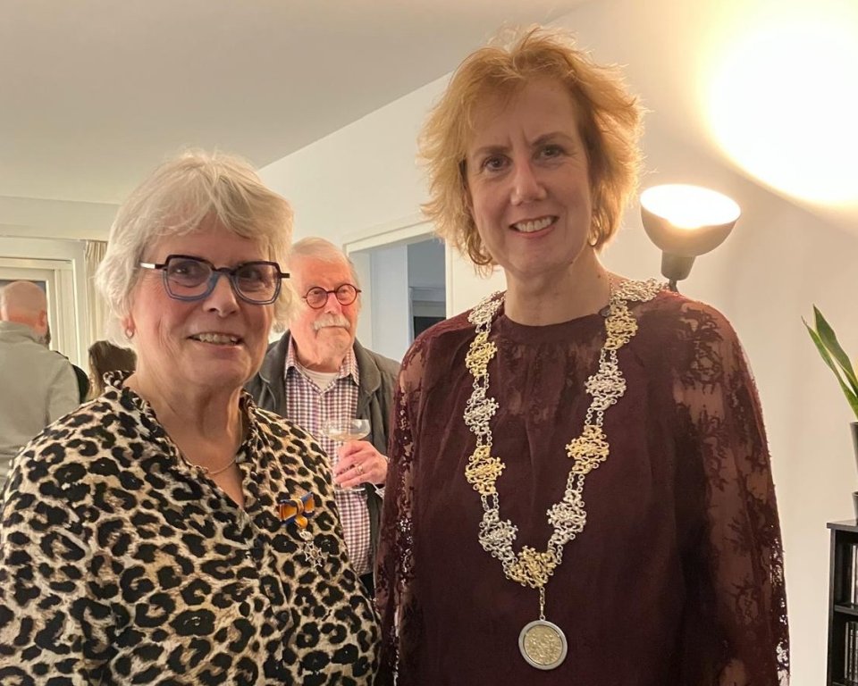 Twee lachende vrouwen, links met een koninklijke onderscheiding, rechts de burgemeester.