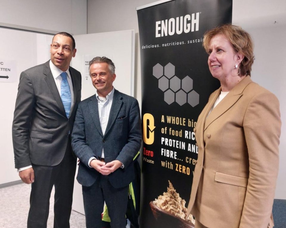 Twee mannen en een vrouw naast een zwarte bannier.