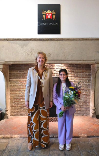 Burgemeester met naast haar de nieuwe kinderburgemeester, zij houdt een bos bloemen vast.