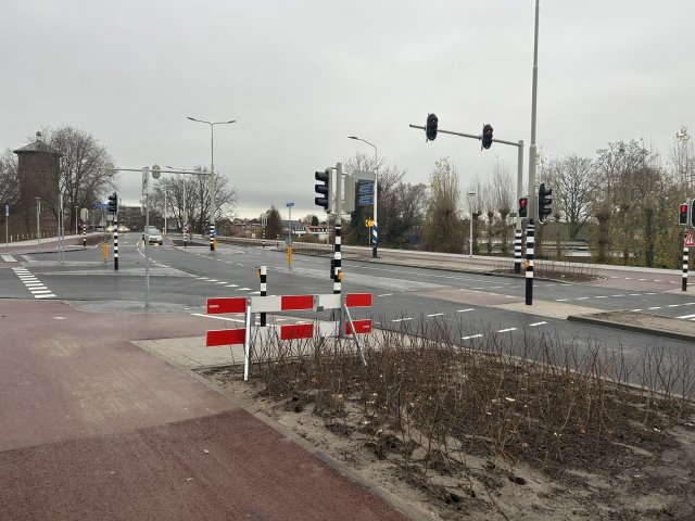 Kruispunt met stoplichten in Bergen op Zoom, op de voorgrond het roodkleurige fietspad en een rood-wit hek.