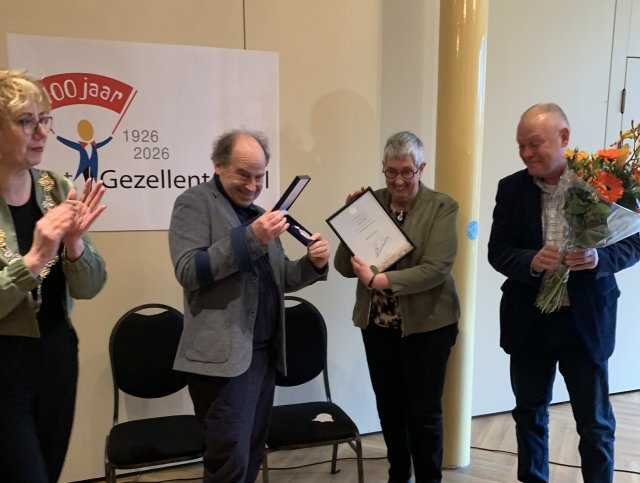 Links de burgemeester, rechts drie leden van het Gezellentoneel die de erepenning, oorkonde en bloemen vasthouden.