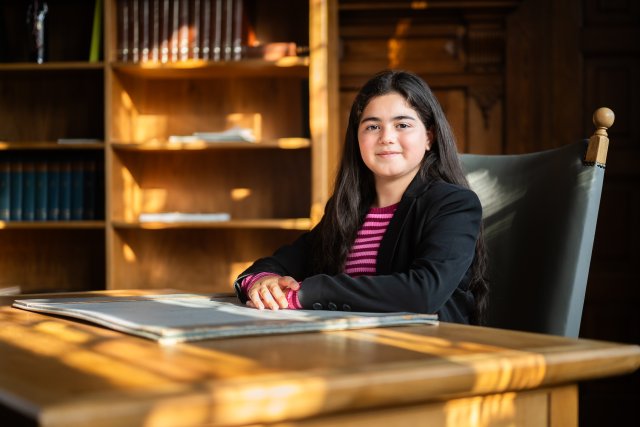 Kinderburgemeester zittend achter een statig houten bureau, op een grijze stoel