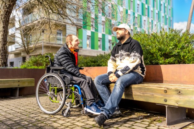 Twee mensen zitten buiten waarvan een persoon in een rolstoel zit