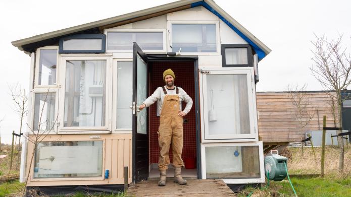 Atse Hamers van Landgoed Rorik staat in deuropening van zelfgebouwd huisje, gemaakt van hergebruikte materialen, waaronder oude deuren en kozijnen