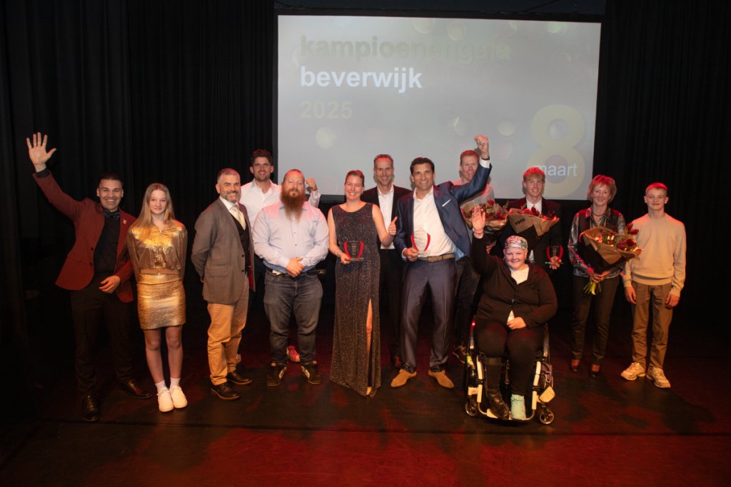 Tien mensen staan naast elkaar onder een groot projectiescherm met de tekst “kampioenengala beverwijk 2025 - 8 maart