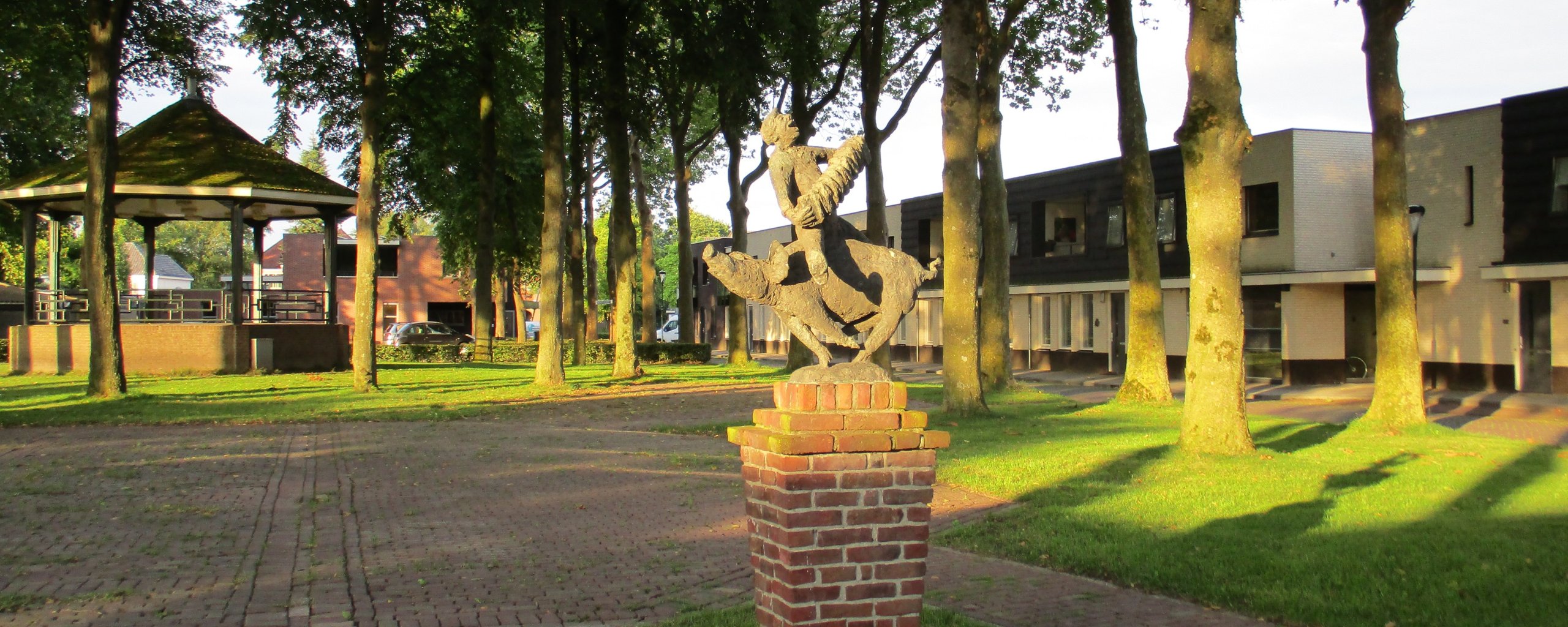 Foto van het Alexanderhof Hapert. Waar het beeld kuuskeskrijer op te zien is en de kiosk. Daarnaast groen inclusief bomen