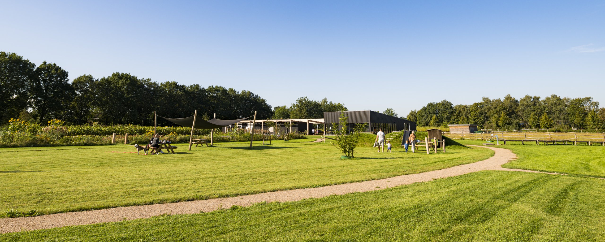 Dorpspark De Groene Long: parkachtige omgeving met mensen die aan picknicktafel zitten met op de achtergrond parkpaviljoen