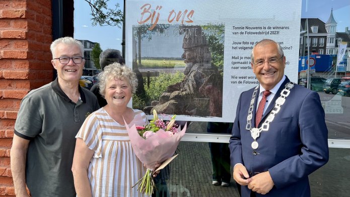 winnares fotowedstrijd van gemeente Bladel staat voor het gemeentehuis van gemeente  Bladel samen met haar man en burgemeester Maurits van den Bosch. Op de achtergrond zie je haar winnende foto