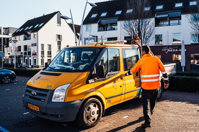 Een medewerker buitendienst van den gemeente loopt naar zijn werkbus met op de achtergrond witte huizen