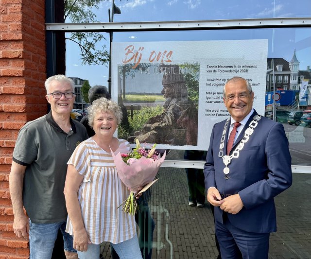 winnares fotowedstrijd van gemeente Bladel staat voor het gemeentehuis van gemeente  Bladel samen met haar man en burgemeester Maurits van den Bosch. Op de achtergrond zie je haar winnende foto