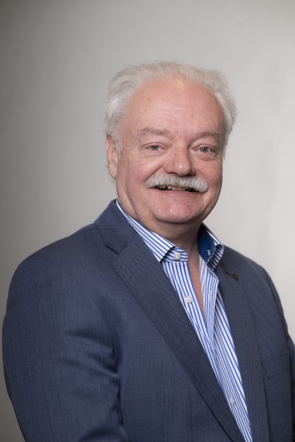 Persoon in donkerblauw jasje poseert voor een neutrale achtergrond