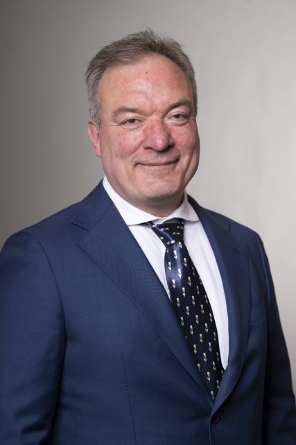 Persoon in een donker maatpak poseert voor een neutrale achtergrond