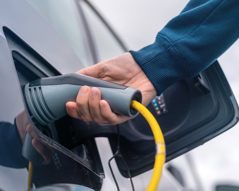 Hand plaatst een gele laadkabel in een elektrische auto.