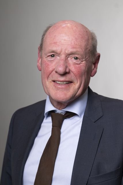 Persoon met donker jasje poseert voor een neutrale achtergrond
