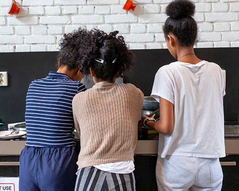 3 jonge meiden met de rug naar de camera, zijn aan het koken