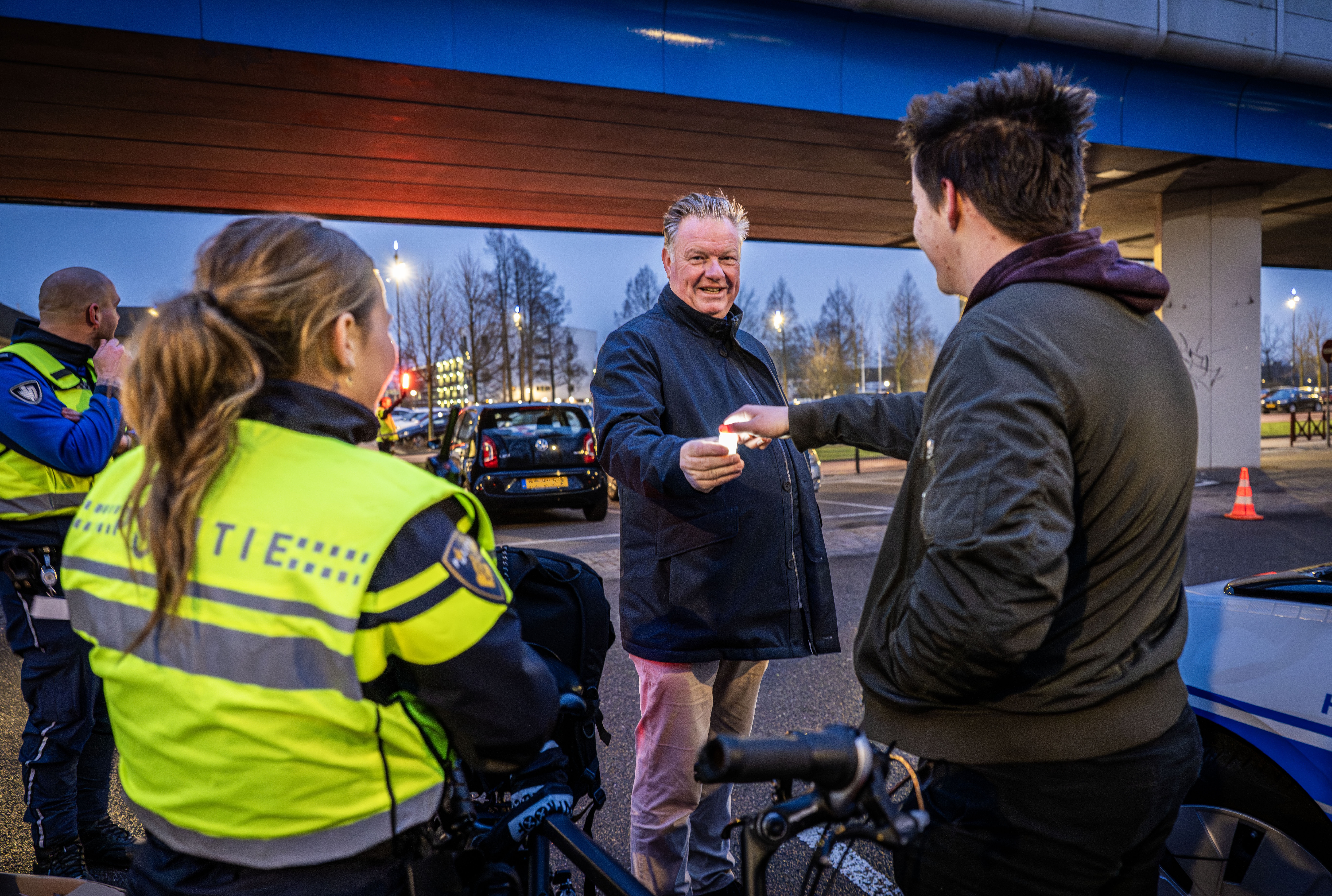 De wethouder deelt een fietslampje uit aan een fietser
