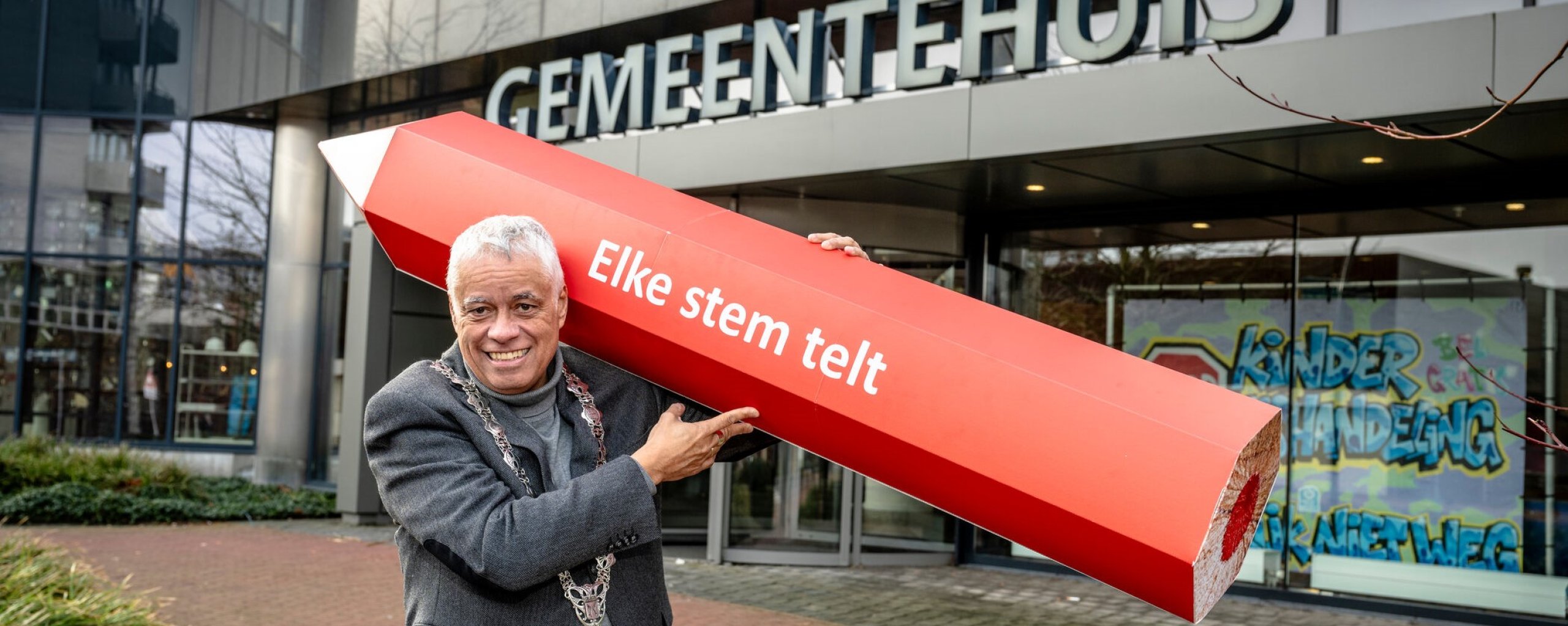 Burgemeester Joost Manusma met een groot rood stempotlood voor het gemeentehuis