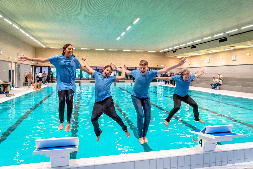 Vier kinderen springen het water in in een binnenzwembad